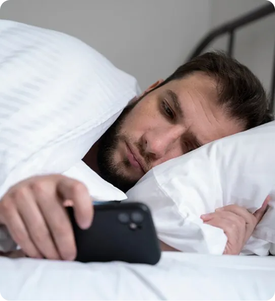 Man awake in bed looking at his phone